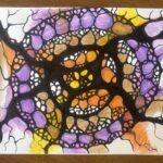 NeuroLotus. A spiral-patterned Neurographica piece with layers of purple, orange, brown, and yellow shapes encircled by black lines. The composition feels like an energetic vortex, with pencils placed on the wooden table as part of the workspace.